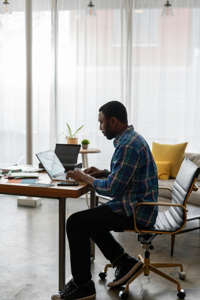 man sitting on chair at desk, working on lap top